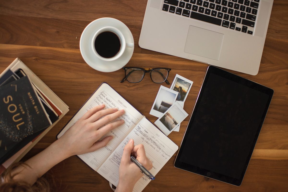 writing in a journal with a laptop and tablet